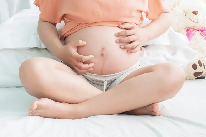 Pregnant woman holding belly while sitting